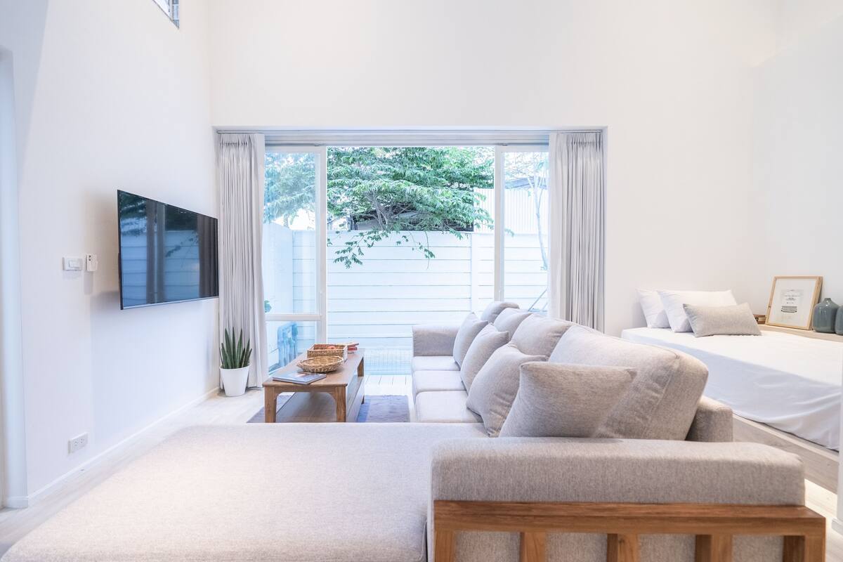 Una habitación moderna con sofá, cama, televisor y ventana con cortinas.
