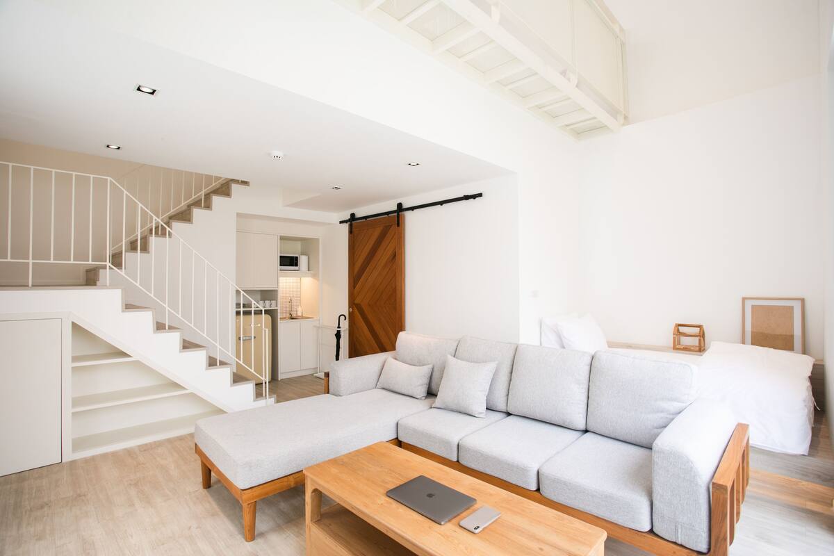 Una sala de estar moderna con un sofá modular, una mesa de centro de madera y una escalera que sube a un nivel superior.