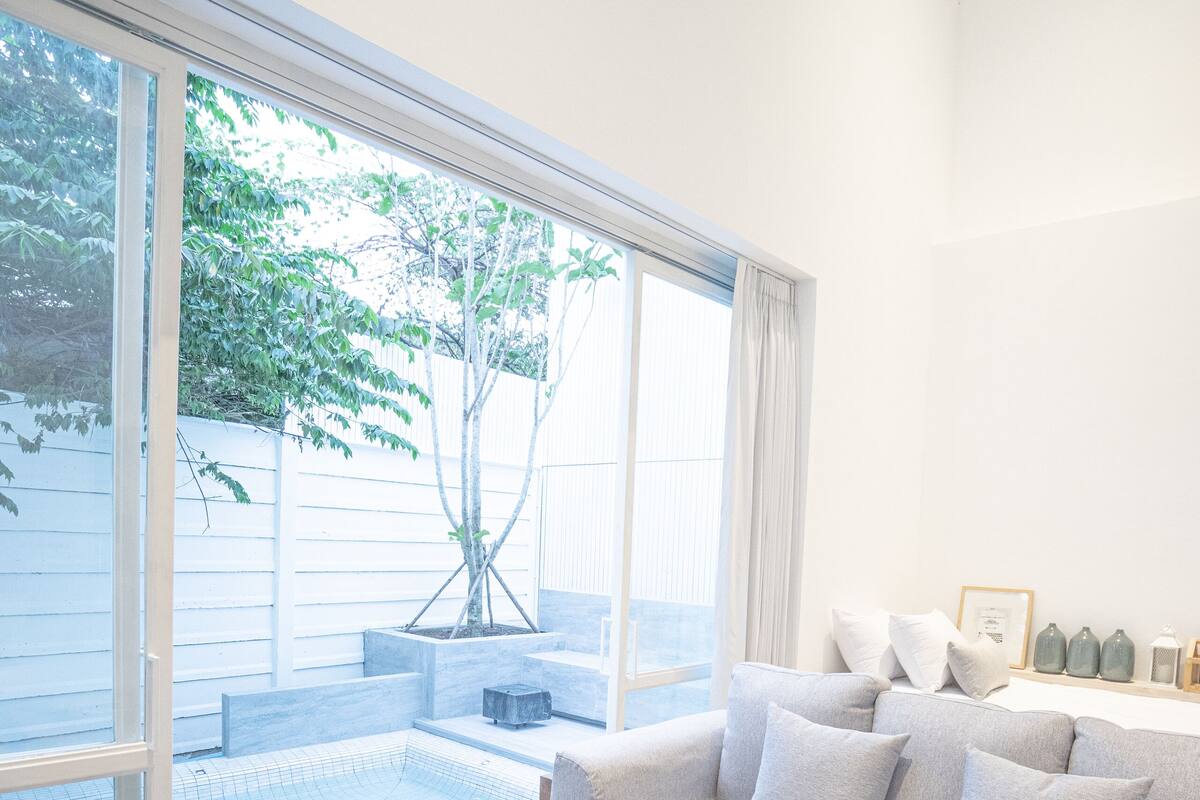 Una sala de estar moderna con un ventanal grande, un sofá gris, una mesa de centro de madera y un pequeño área de piscina.