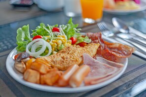 Prato de comida de café da manhã com ovos, bacon, presunto, batatas e uma salada com diversos vegetais.
