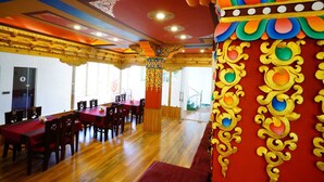 A dining area with wooden tables and chairs, a red carpet, and ornate golden and colorful wall decorations. - The Shanti Nest At Boutique Hotel (Leh)