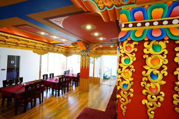 A dining area with wooden tables and chairs, a red carpet, and ornate golden and colorful wall decorations.