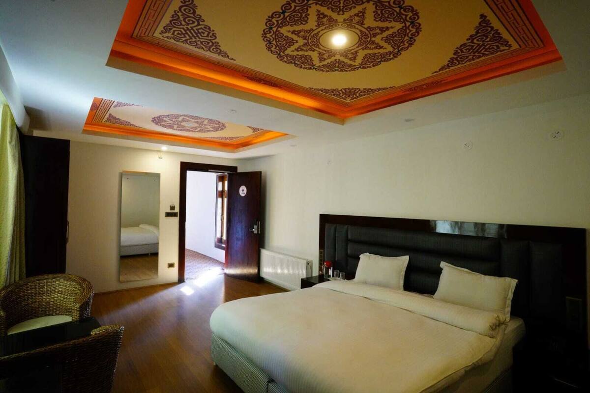 A hotel room with a large bed, a chair, a mirror, and a decorative ceiling.