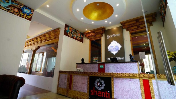 A reception area with a modern design, featuring a central circular light fixture, a reception desk with a logo, and a wall-mounted sign. - The Shanti Nest At Boutique Hotel (Leh)