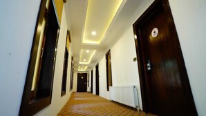 A long, narrow hallway with a patterned carpet, wooden doors, and recessed ceiling lighting. - The Shanti Nest At Boutique Hotel (Leh)