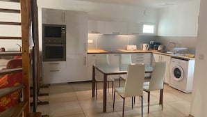 A modern kitchen with white cabinets, a built-in oven, a microwave, a washing machine, and a dining area with a table and chairs. - Gite de charme 4 a 7 pers (Albaron)