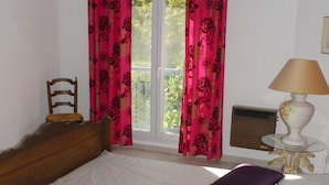 A bedroom with a wooden bed, a purple pillow, a white lamp, and a window with pink curtains. - Gite de charme 4 a 7 pers (Albaron)