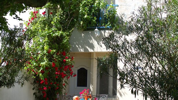 A white building with a tiled roof, a balcony, and a table with chairs outside. - Gite de charme 4 a 7 pers (Albaron)