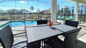 An outdoor patio with a pool, covered seating area, and a table with chairs.