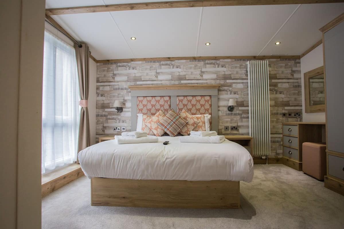 A bedroom with a large bed, wooden headboard, and a stone-patterned wall.