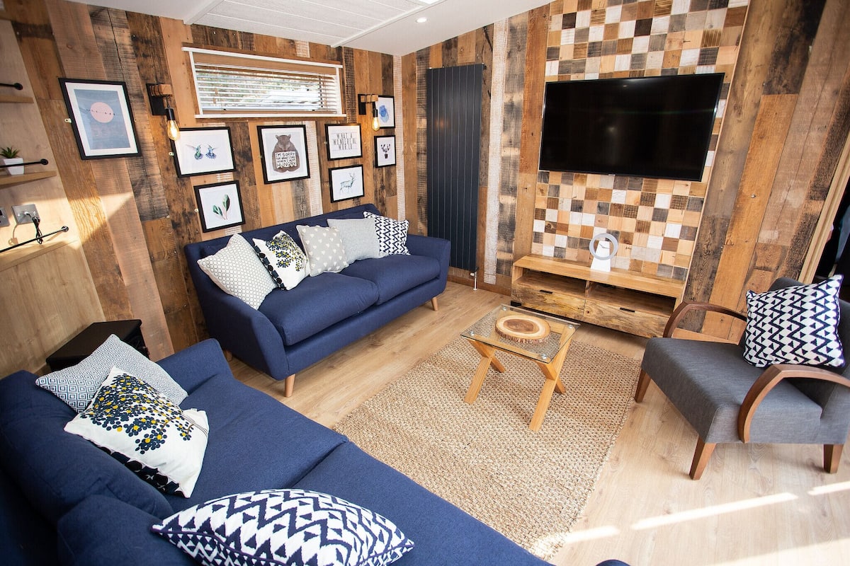 A living room with a blue sofa, a wooden coffee table, and a TV mounted on a wooden wall.