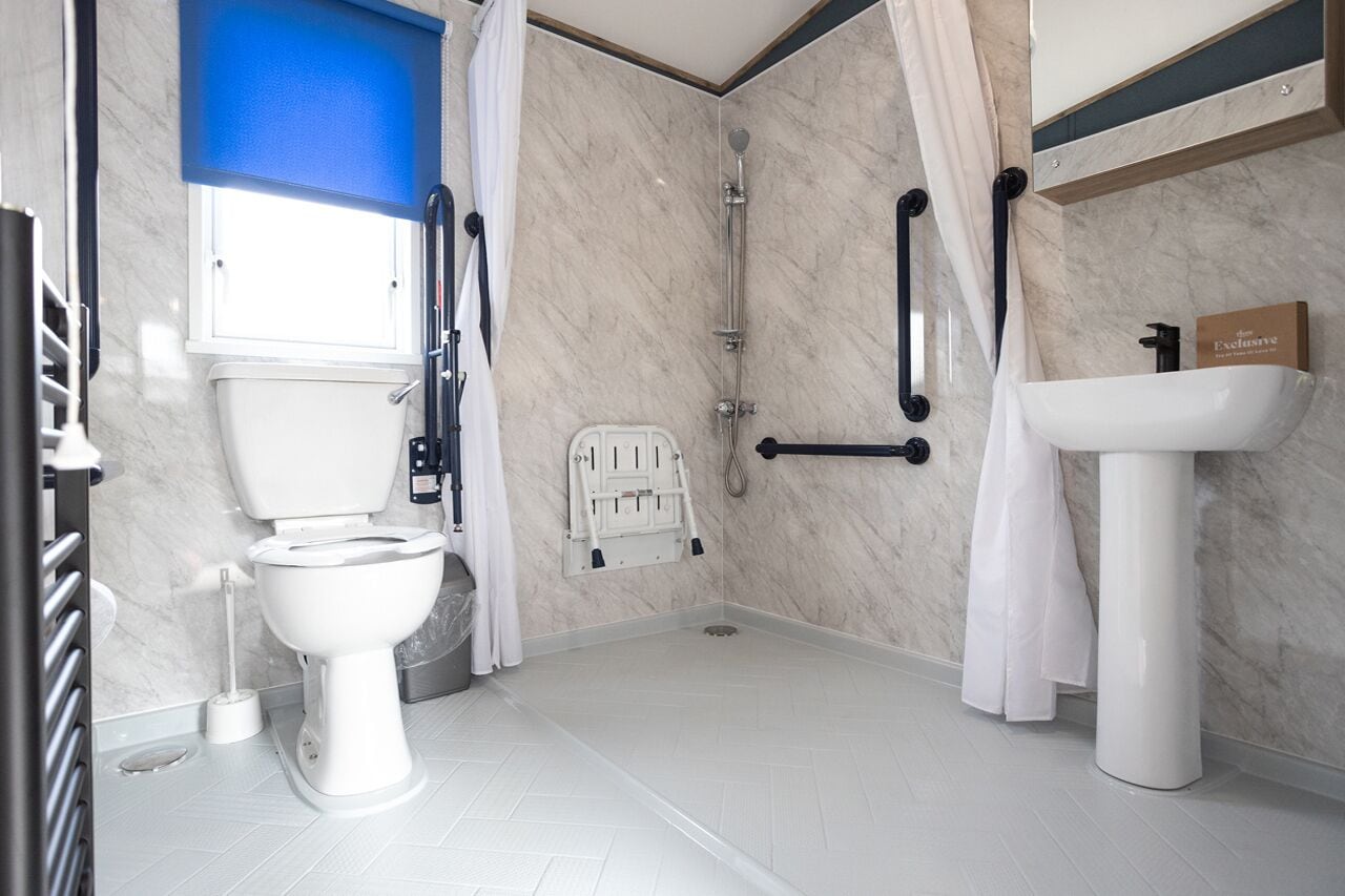 A modern bathroom with a white toilet, a shower with a glass door, a white sink, and a blue window.