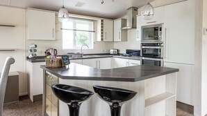 A modern kitchen with a central island, stainless steel appliances, and pendant lighting. - Sandy Balls  Holiday Village (Fordingbridge)