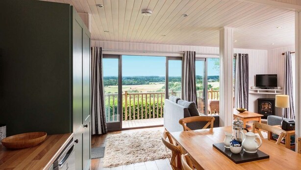 A spacious living area with a large window overlooking a scenic landscape, a dining area with a wooden table, and a cozy seating arrangement. - Sandy Balls  Holiday Village (Fordingbridge)