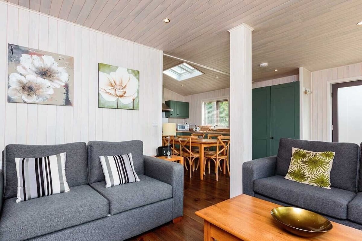 A modern living room with two grey sofas, a wooden coffee table, and a dining area with a green cabinet and a window.