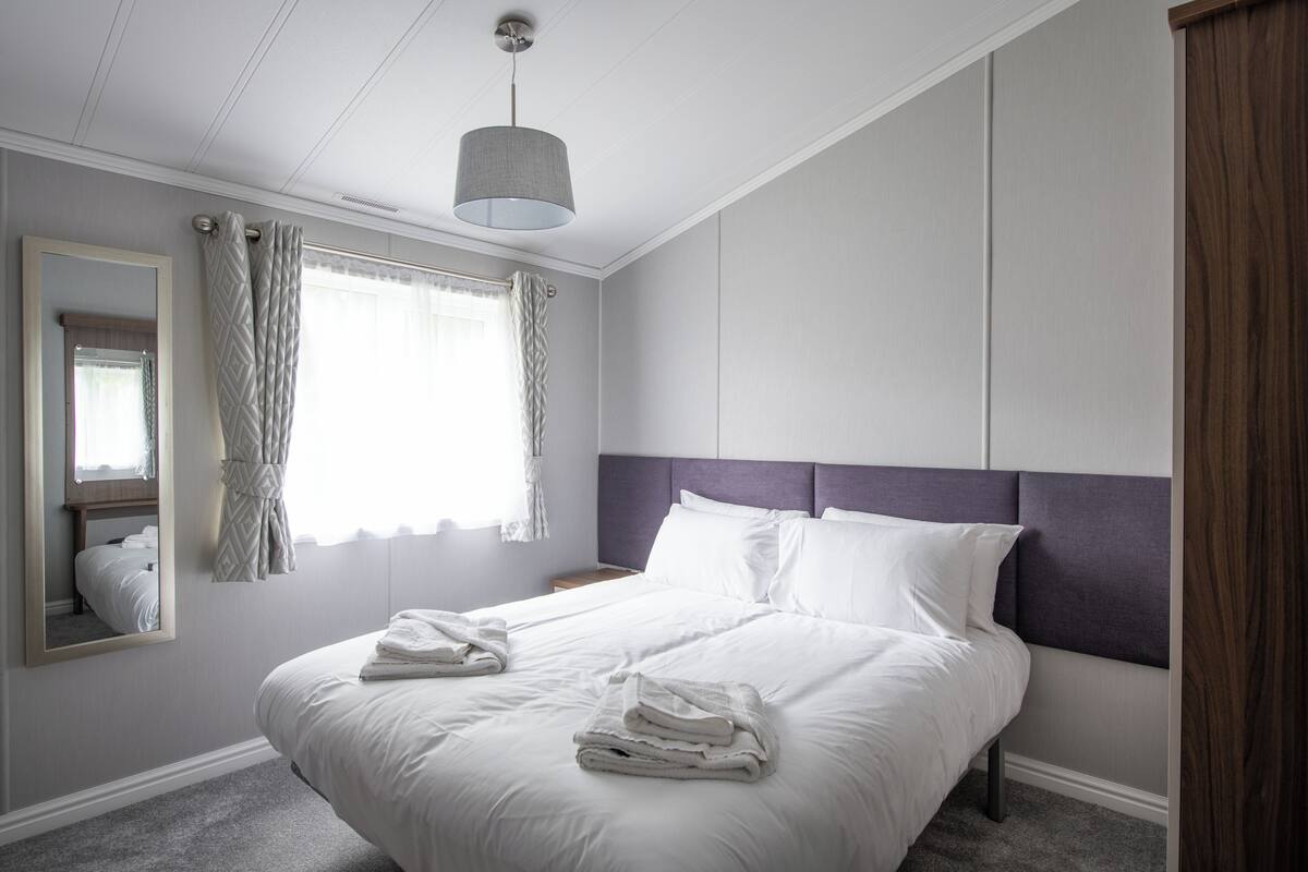 A hotel room with a large bed, a bedside table, a mirror, and a window with curtains.