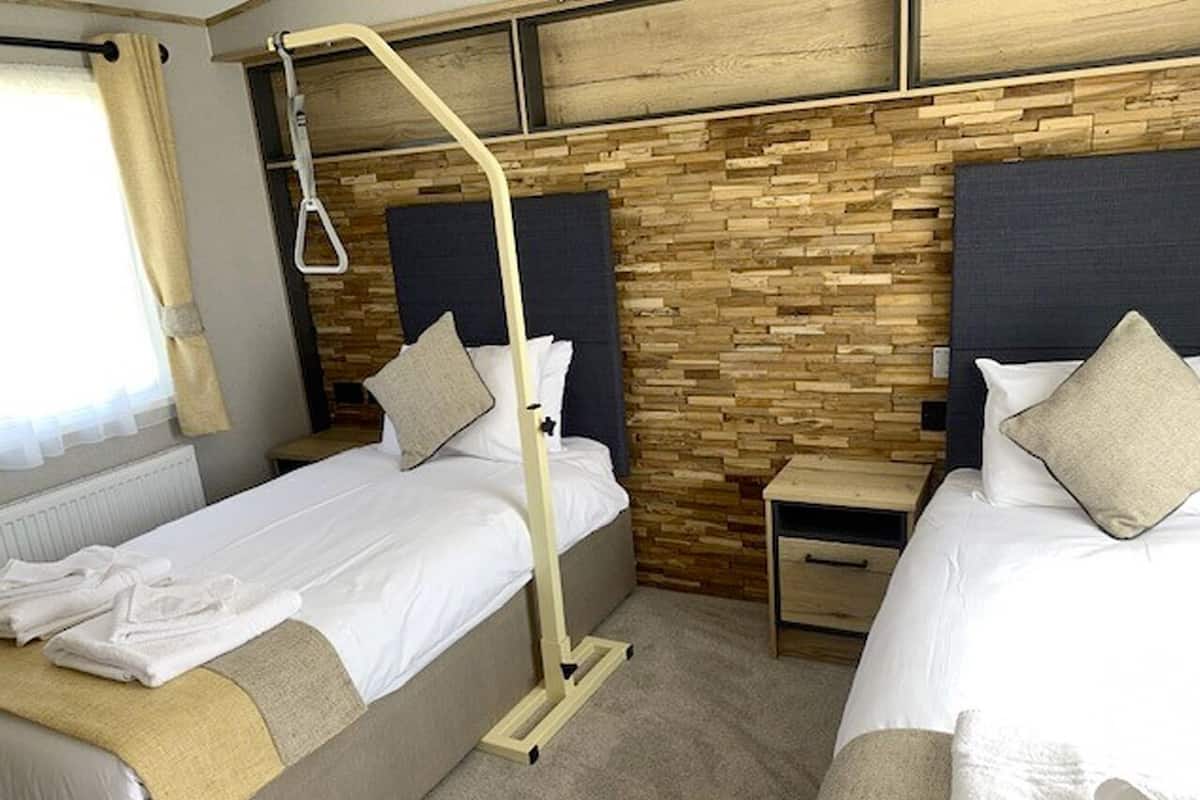 A hotel room with two beds, wooden wall paneling, bedside tables, and a window with curtains.