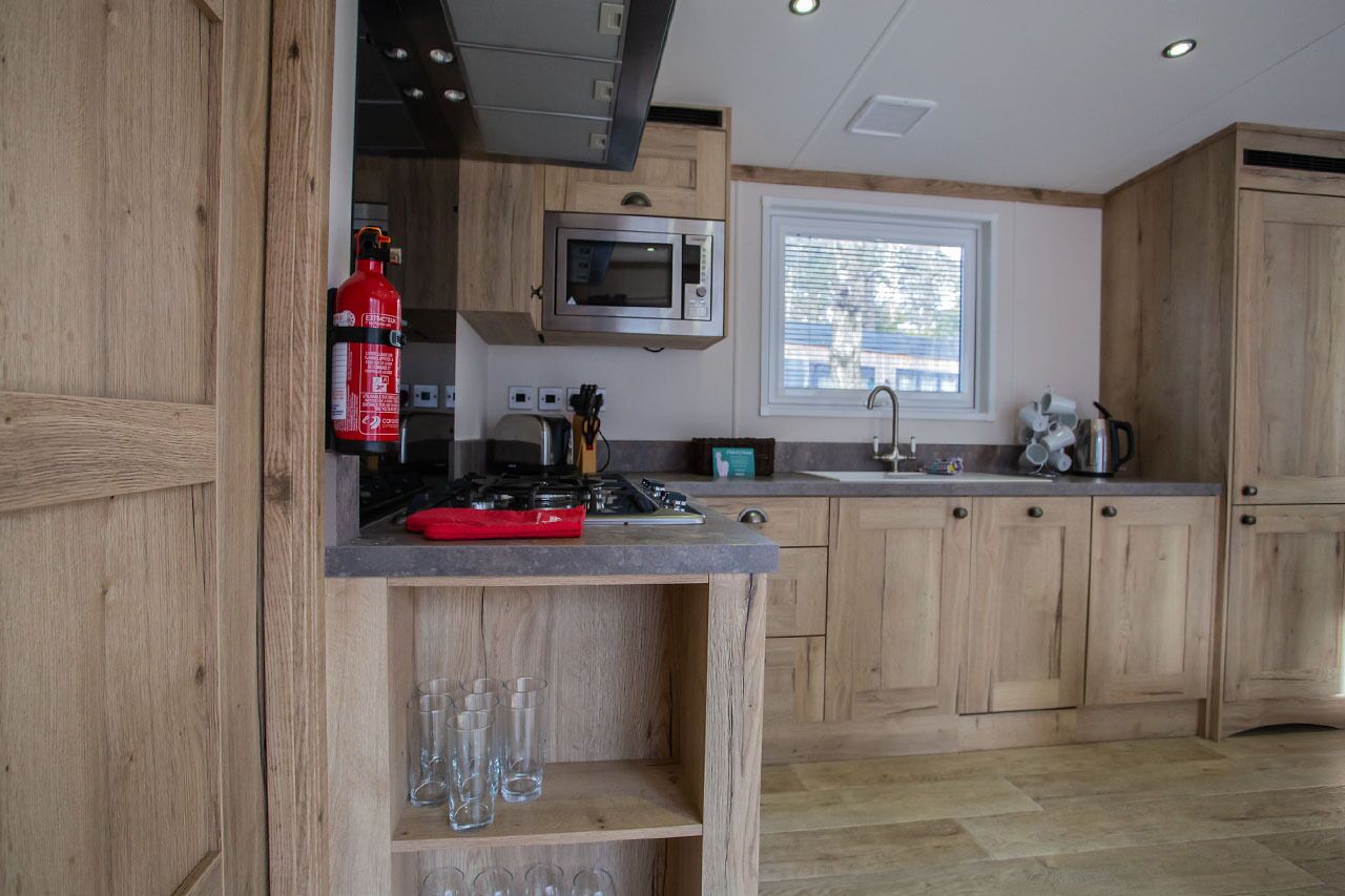 Une cuisine moderne avec des meubles en bois, un four à micro-ondes, une cuisinière à gaz et une fenêtre équipée de stores.