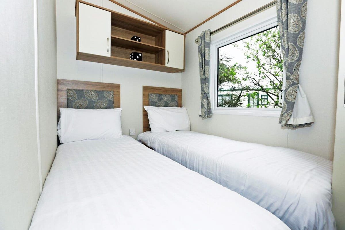 A bedroom with two single beds, a built-in shelf with dice, and a window with curtains.