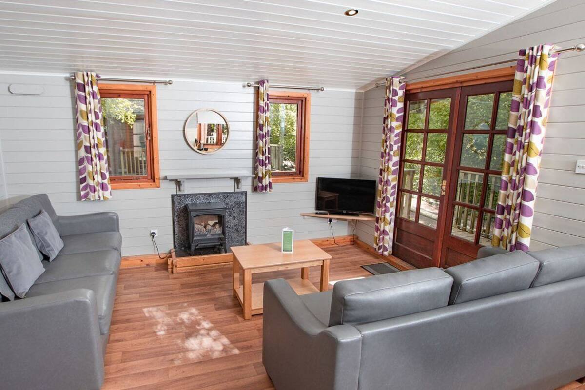 A cozy living room with a fireplace, grey sofas, a TV, and a wooden table.