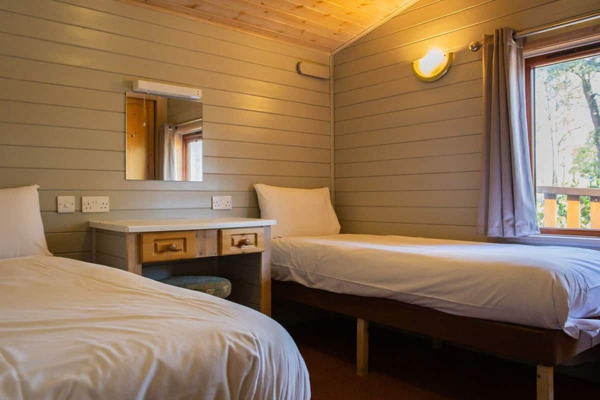 A room with two beds, a small table with drawers, a mirror, and a window with curtains.
