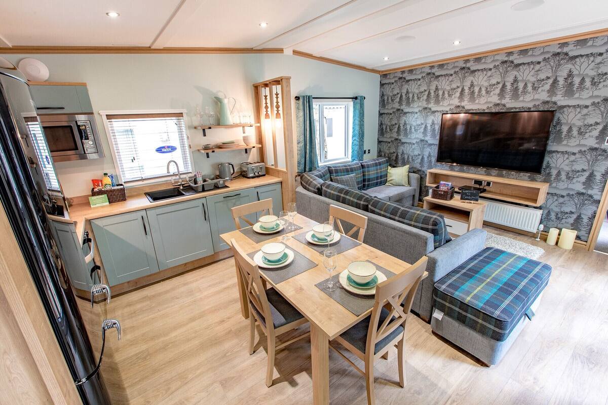 A modern kitchen with a microwave, sink, and dining area with a table set for four. There is a sofa and a television in the living area.