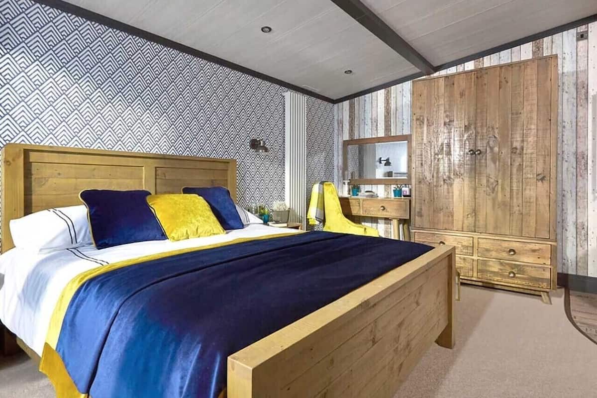 A bedroom with a wooden bed, a nightstand, a wardrobe, and a patterned wallpaper.