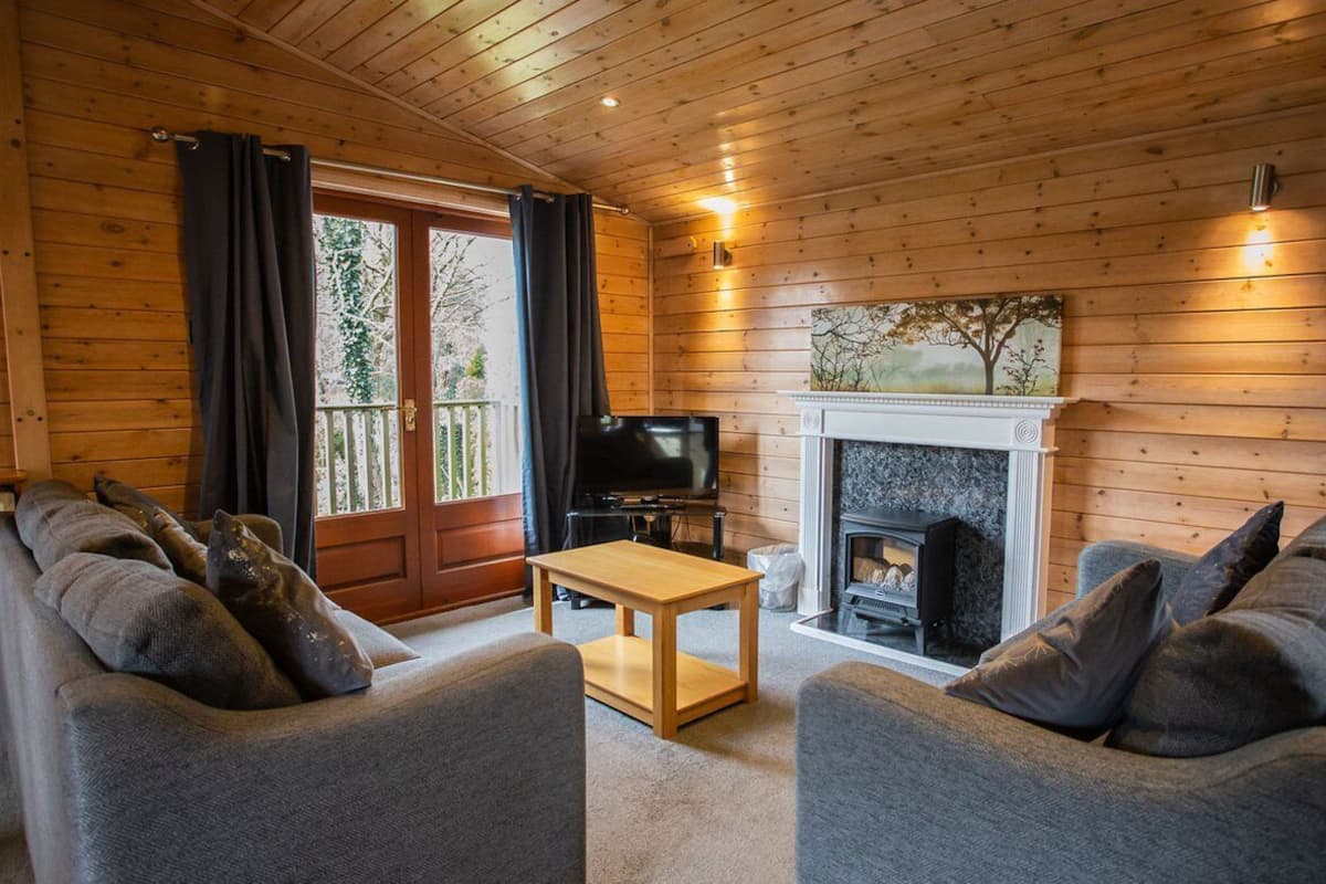 A cozy cabin interior with two grey sofas, a wooden table, a fireplace, and a TV.
