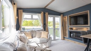 A cozy living room with a sofa, a flat-screen TV, and a fireplace. - Sandy Balls  Holiday Village (Fordingbridge)