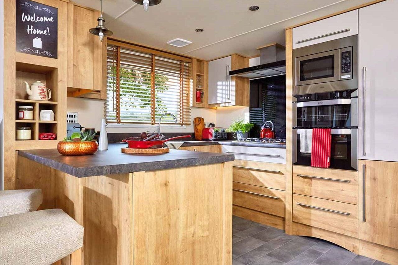 A modern kitchen with wooden cabinets, a central island, and built-in appliances including a microwave and oven.