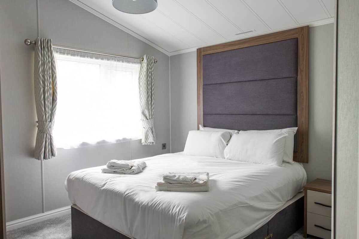 A neatly made bed with folded towels, a wooden headboard, and a small bedside table with drawers.