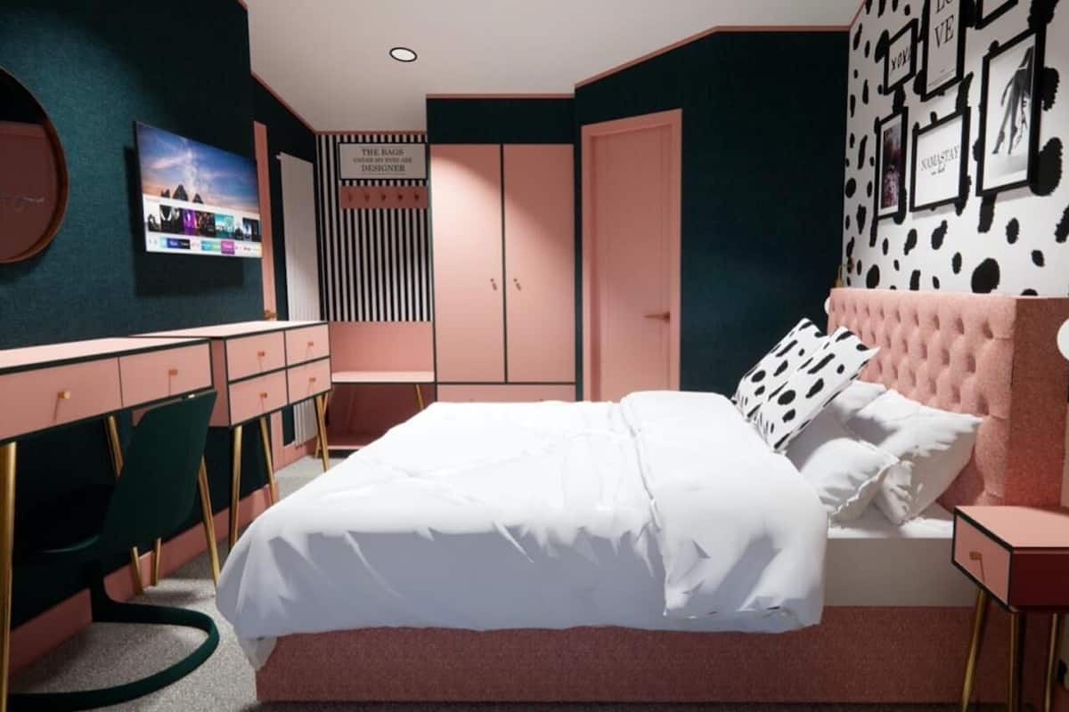 A bedroom with a bed, a desk, a chair, a wardrobe, and a TV on the wall.
