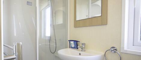 Une salle de bain avec une douche à parois de verre, un lavabo blanc et un miroir au-dessus.