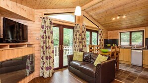 A wooden cabin interior with a sofa, TV, and kitchen area. - Sandy Balls  Holiday Village (Fordingbridge)