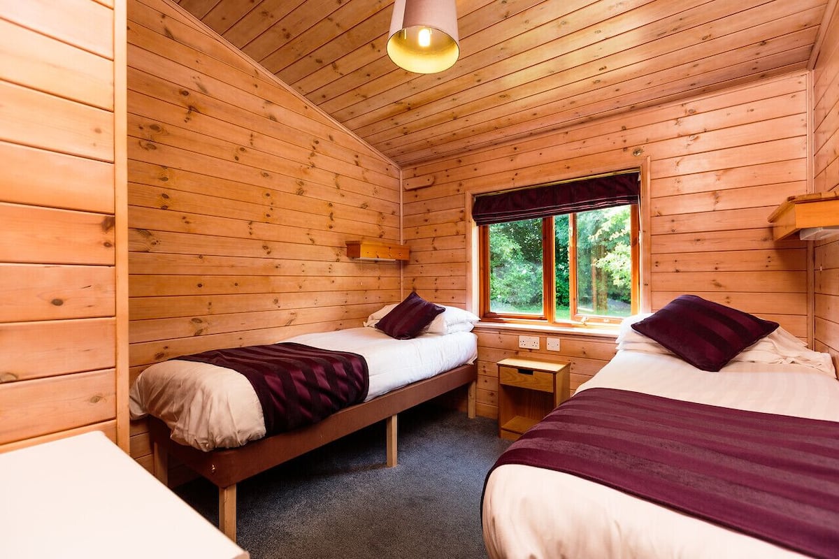 A wooden cabin room with two beds, a window, and a small table.