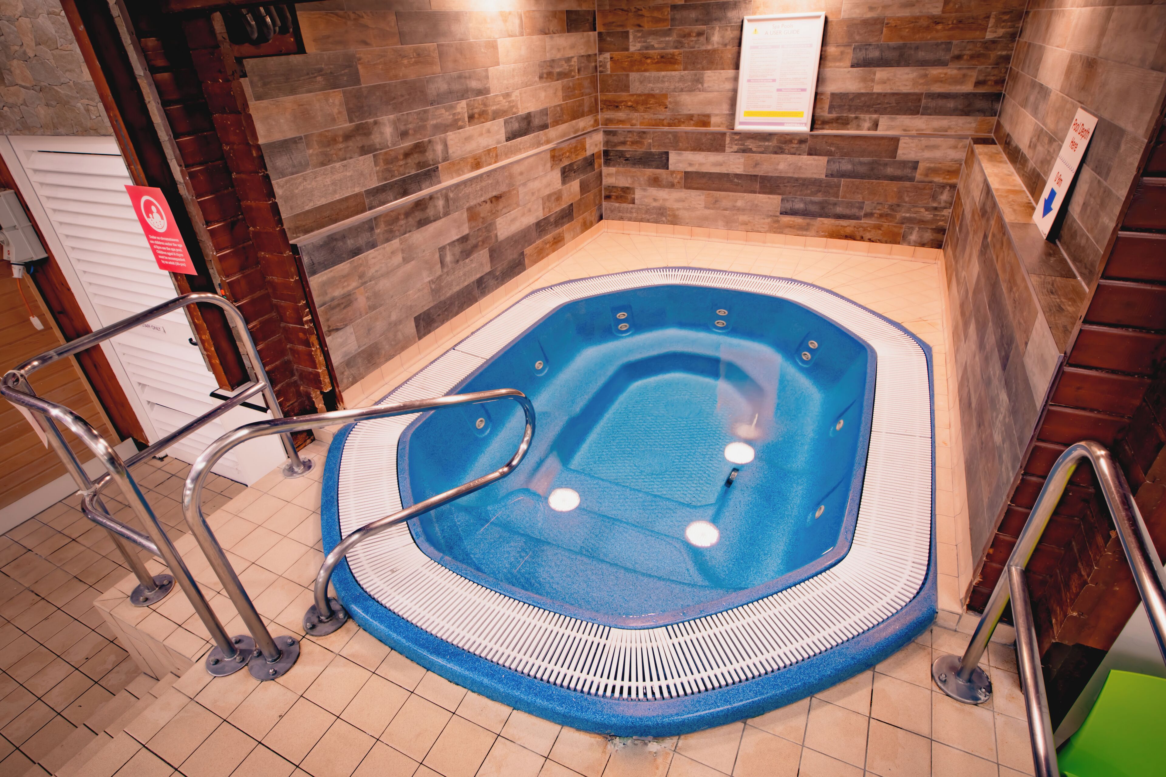 Un jacuzzi con barandas de metal, piso de baldosas y paredes de madera.