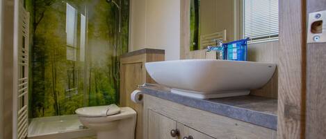 Un baño con inodoro blanco, un lavamanos grande de color blanco y un dosificador de jabón azul, y una zona de ducha con puerta de cristal.