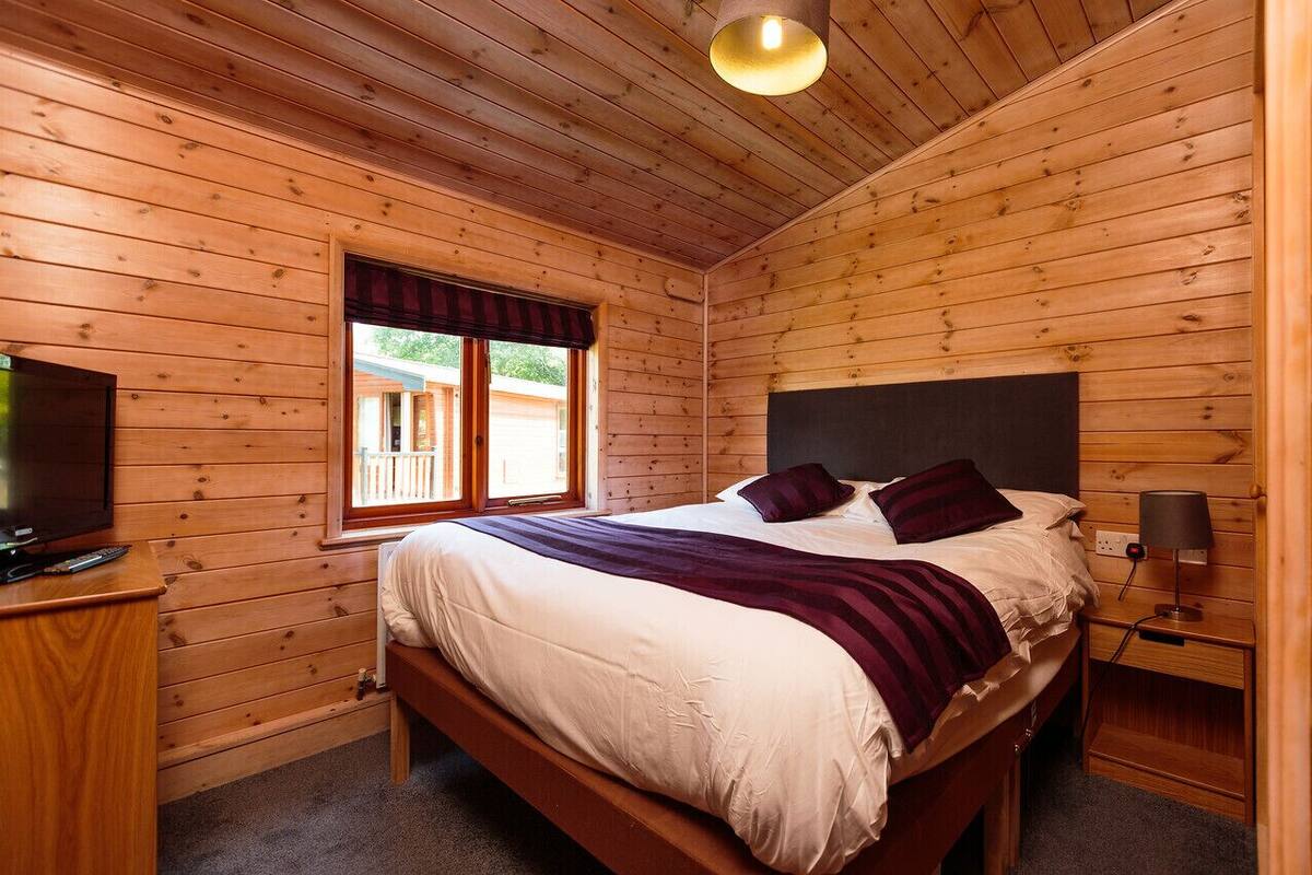 A wooden cabin bedroom with a bed, a TV, and a window.