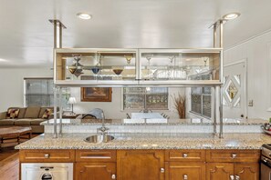 A kitchen with granite countertops, wooden cabinets, a stainless steel sink, and a built-in glass-fronted upper kitchen area.