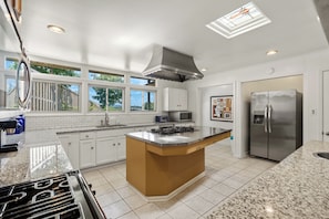 A modern kitchen with white cabinets, a central island, stainless steel appliances, and a skylight.