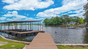 A wooden dock leading to a covered pier with benches, a lake, and houses in the background. - Spectacular House on Lake Hamilton (Lake Hamilton)