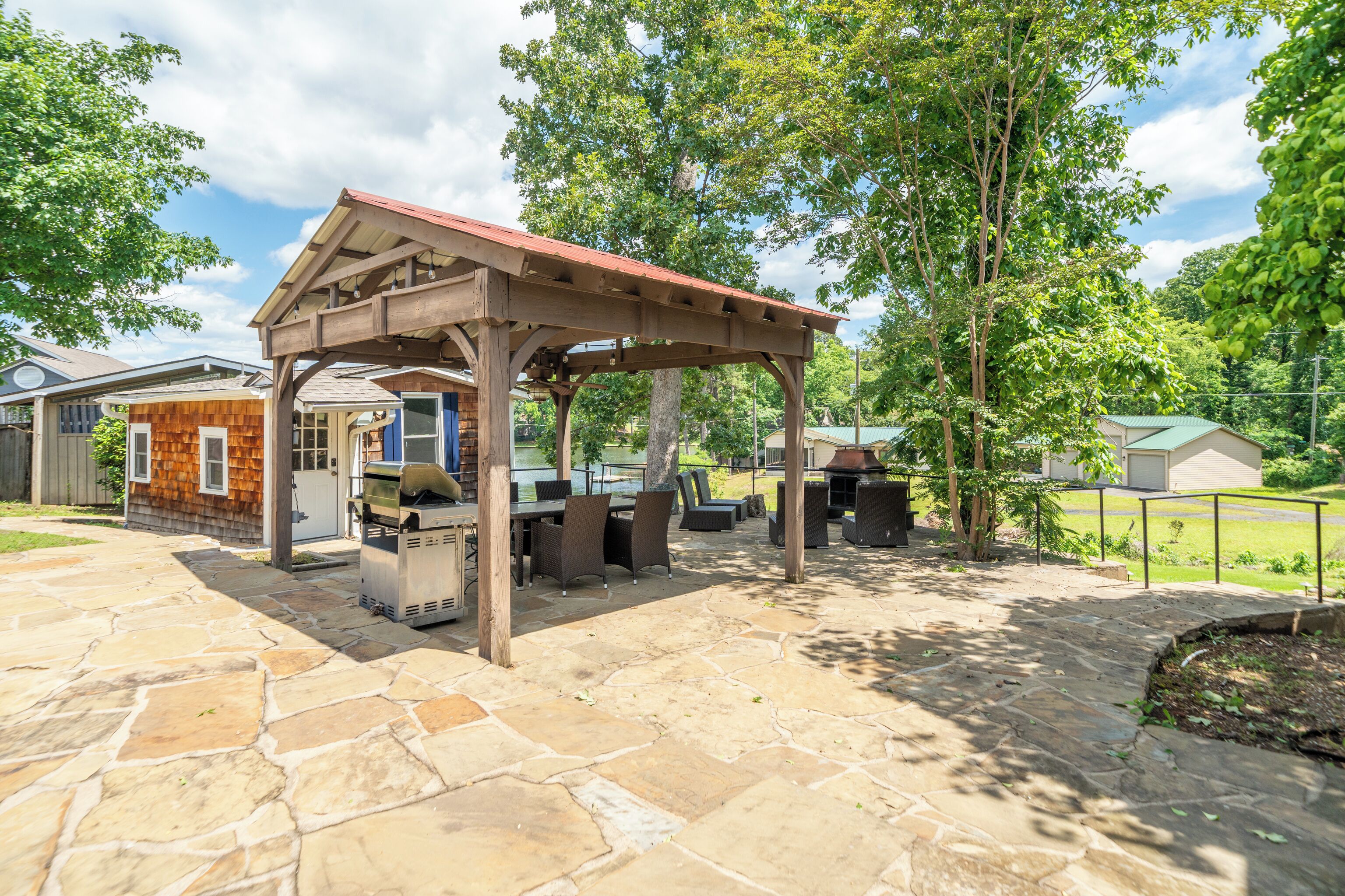 A stone patio with a wooden pergola, outdoor seating, and a grill area.