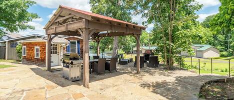 A stone patio with a wooden pergola, outdoor seating, and a grill area.