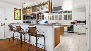 A modern kitchen with white cabinetry, a central island with bar stools, stainless steel appliances, and a stained glass window. - Spectacular House on Lake Hamilton (Lake Hamilton)