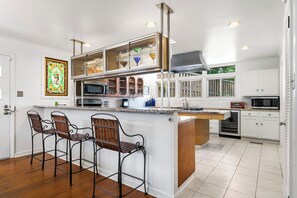 A modern kitchen with white cabinetry, a central island with bar stools, stainless steel appliances, and a stained glass window.
