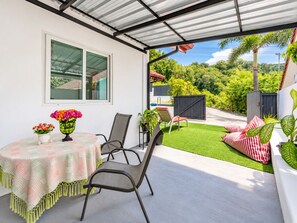 Un patio al aire libre con una mesa, sillas y vistas a un exuberante jardín.