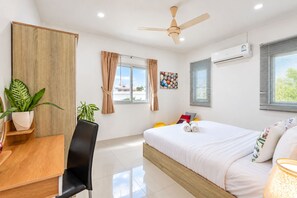 Una habitación de hotel moderna con cama, escritorio, silla, ventilador de techo, equipo de aire acondicionado y ventana con cortinas.