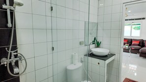 Un baño con azulejos blancos, un lavamanos blanco y una ducha con manguera.