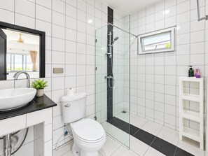 A modern bathroom with a glass-enclosed shower, a white toilet, a sink with a mirror above, and a small shelf with toiletries. - Star villa 2 bedrooms /Private swimming pool for family (Tambon Chalong)