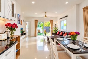 A modern kitchen with a dining area, a sofa, and a view of the garden. - Star villa 2 bedrooms /Private swimming pool for family (Tambon Chalong)